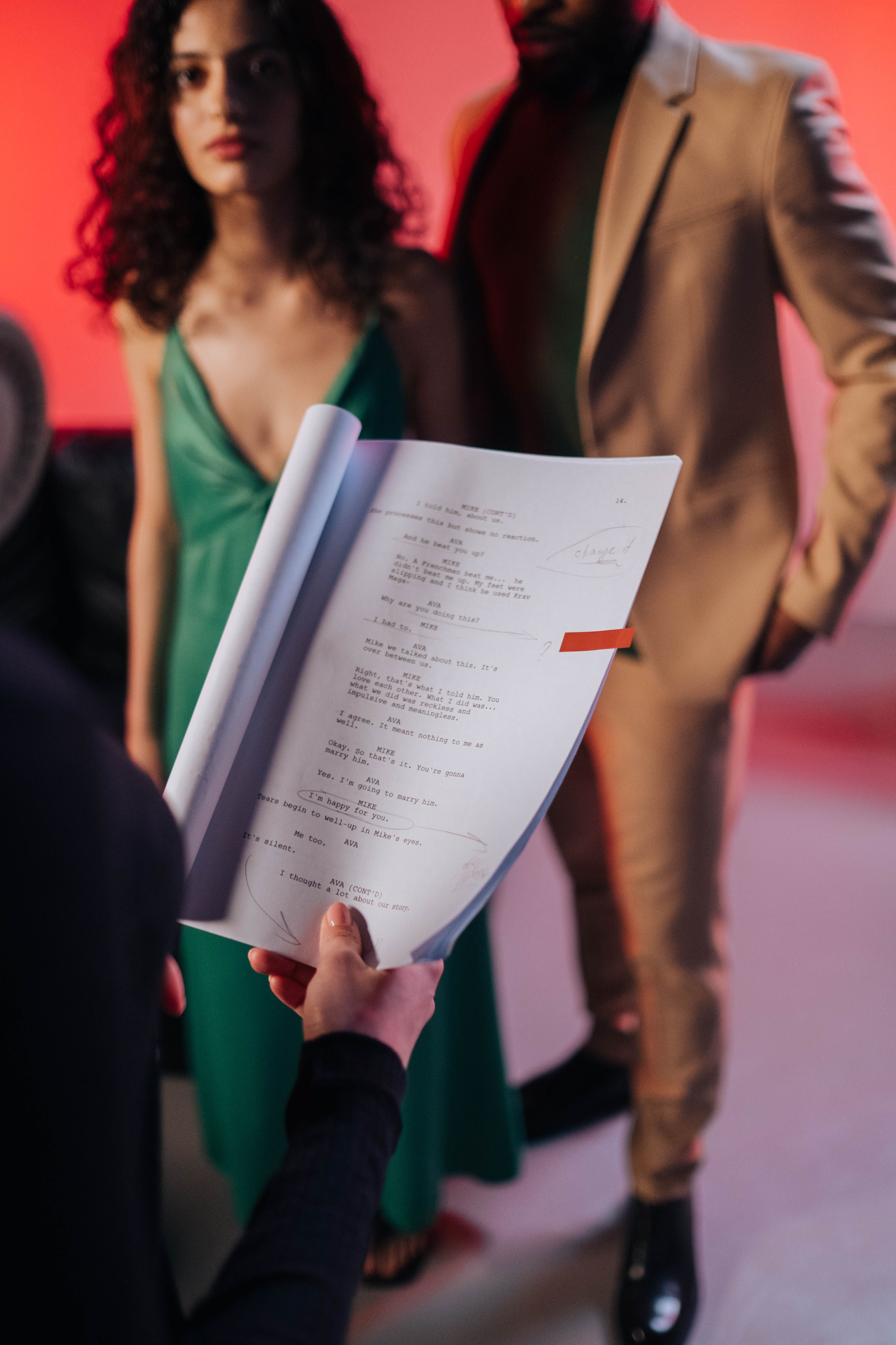 A hand holds annotated screenplay pages in front of two performers during a rehearsal.